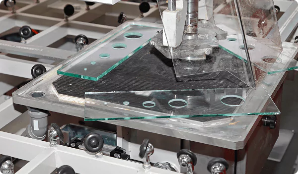 Glass cutting machine shaping tempered glass sheets with precision holes on a production line.